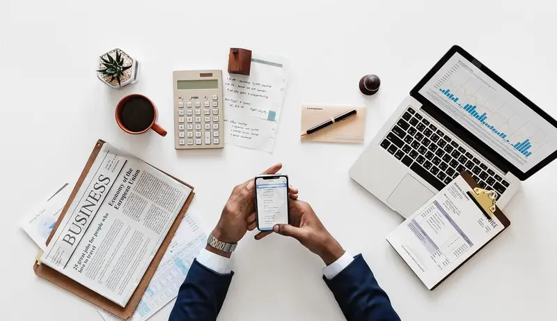 Werkplek van bovenaf met laptop, rekenmachine, koffie en smartphone
